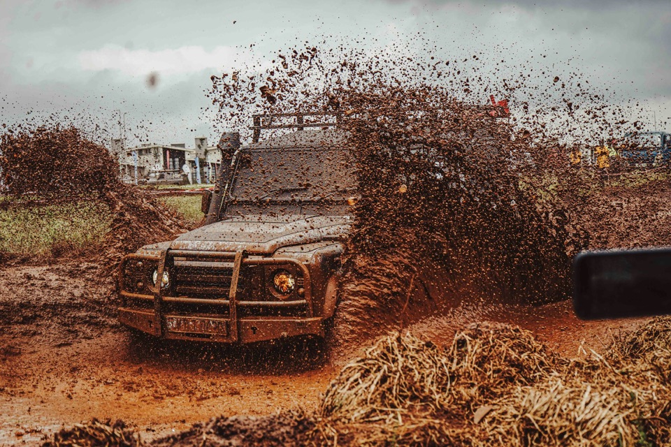 A mud-covered Land Rover Defender throwing a wall of wet mud into the air as it powers through a rutted track