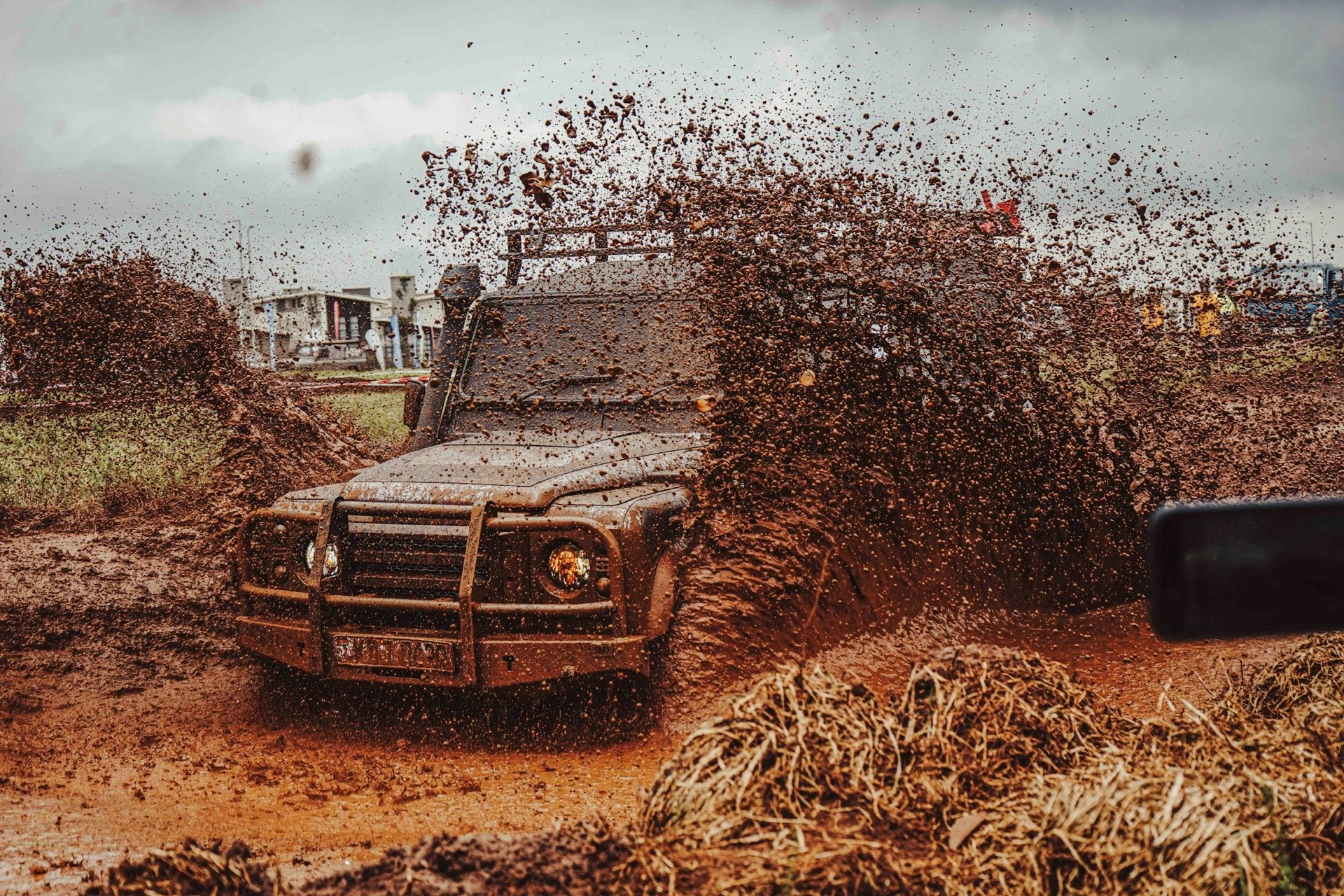 A mud-covered Land Rover Defender throwing a wall of wet mud into the air as it powers through a rutted track